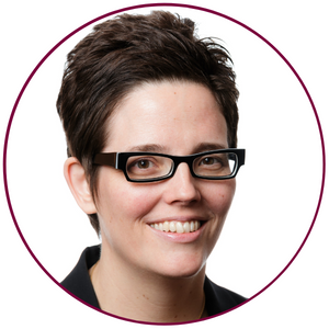 A tight headshot of Sara Bannerman. She is wearing black thick-rimmed glasses and is smiling at the camera.