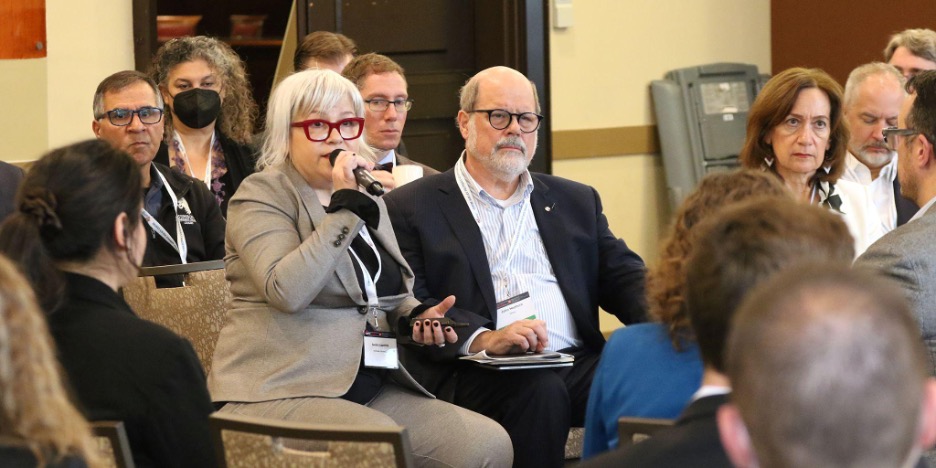 A seated woman holding a mic, besides 2 other people.