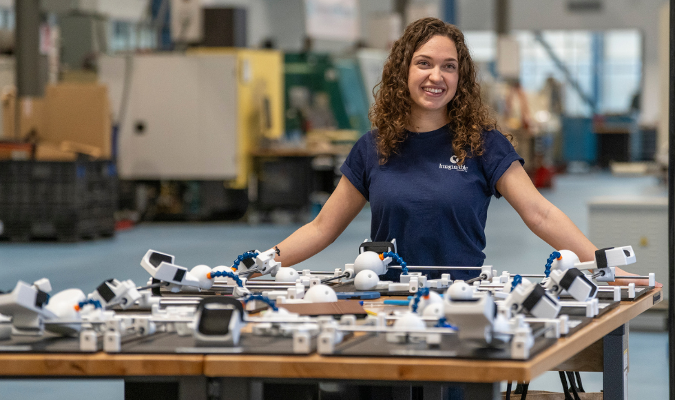 Lianna Genovese standing at a waist-high table covered in industrial parts of Guided Hands.