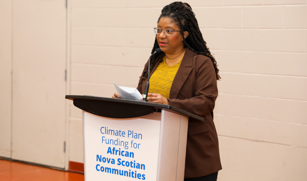 Ingrid Waldron speaking in to a microphone at a podium. 