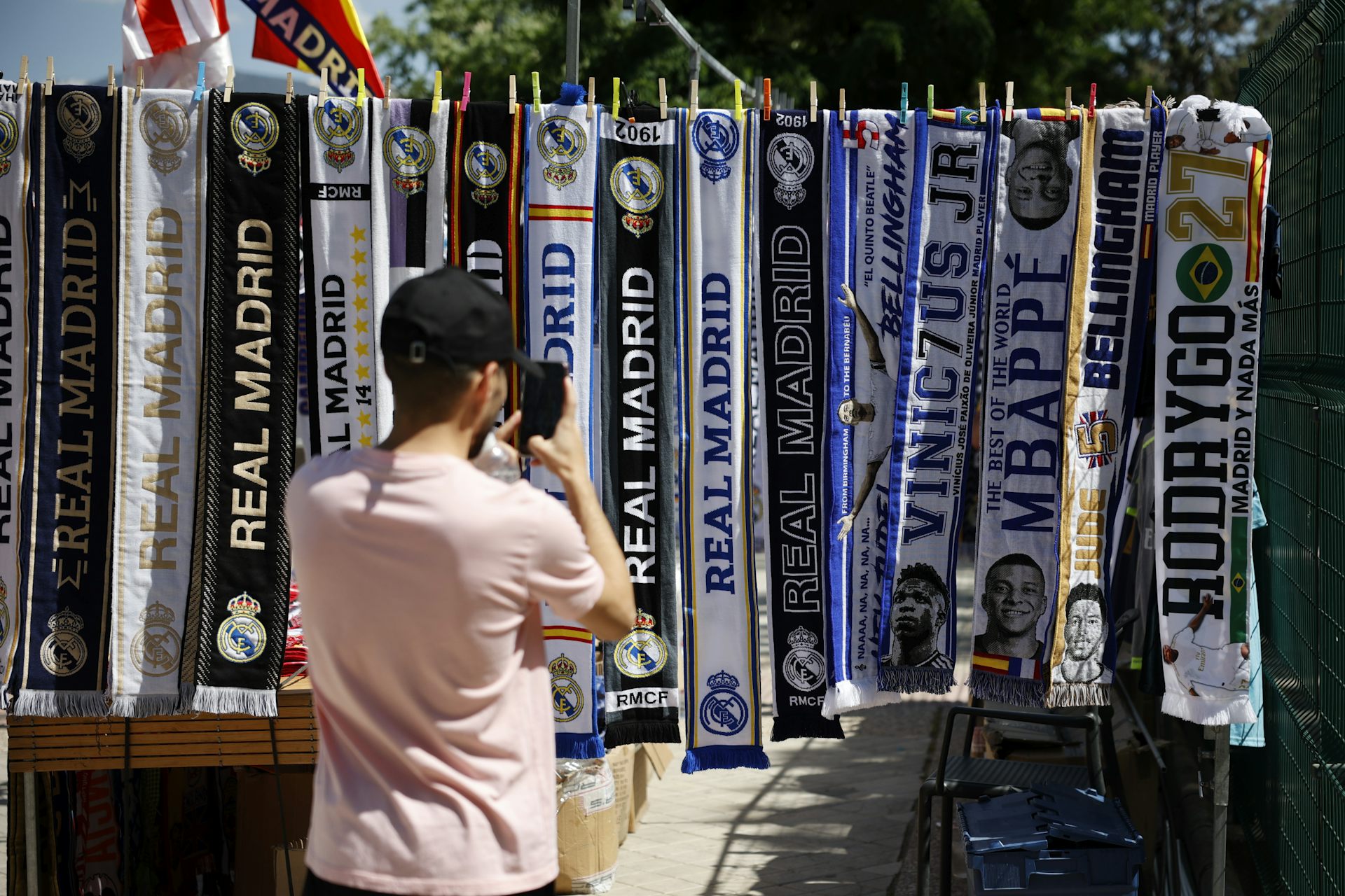 "A man takes a photo of scarves with soccer team names printed on them hanging from a clothes line"