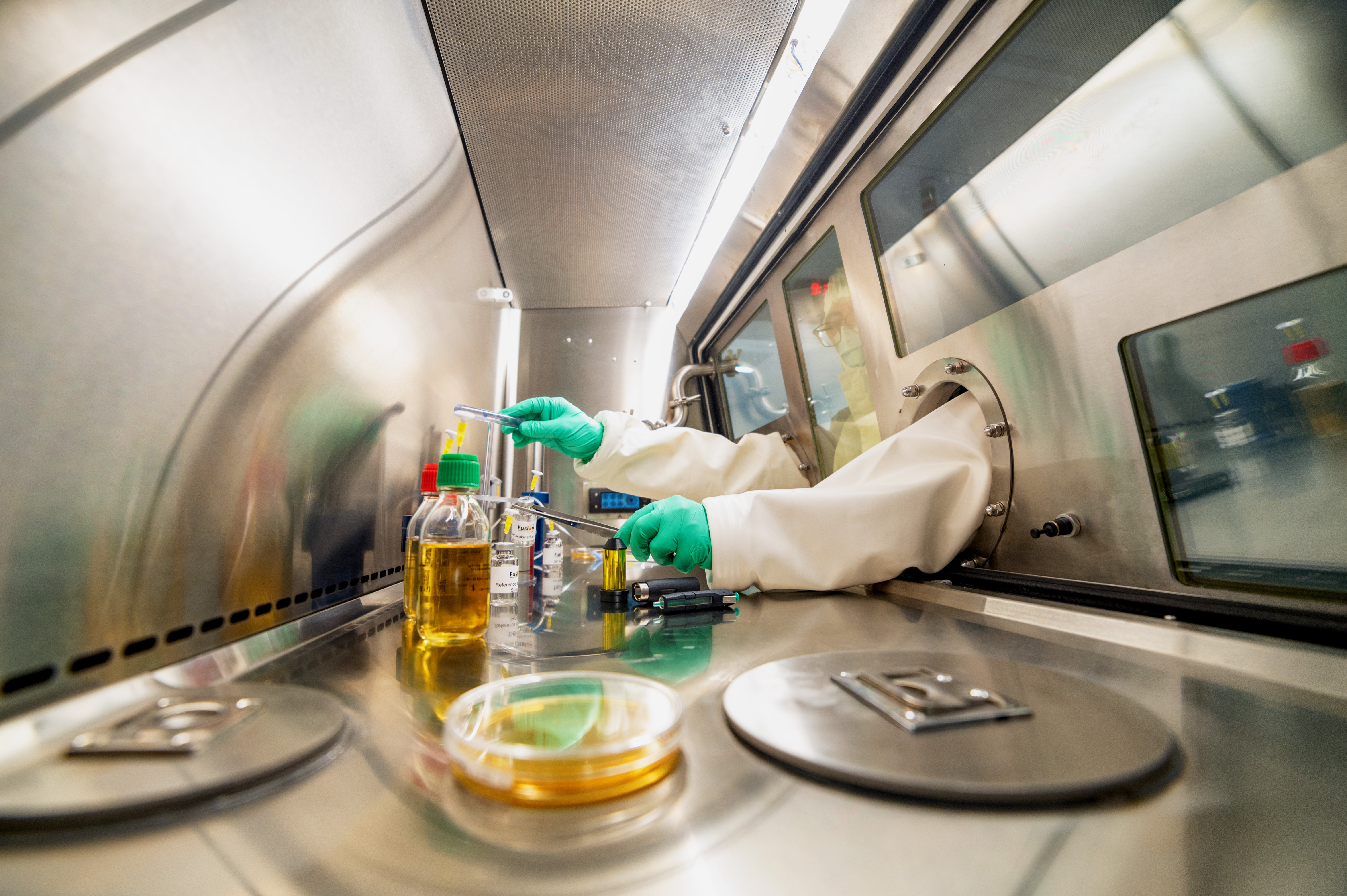 Inside a hot cell, or containment chamber, a person's gloved hands work with medical isotopes.