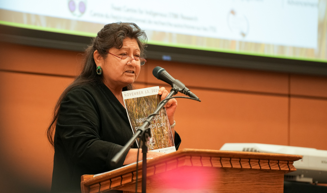 Elder Dixie Doxtator holds up the Indigenous Research Day program at the podium