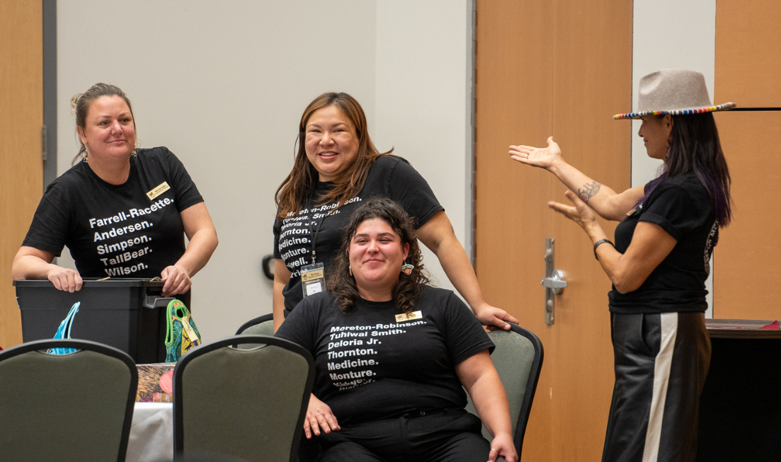 MIRI director savage bear gestures at organizers of MIRI Research Day 2024. All are wearing black "Names in Indigenous Research" T shirts.