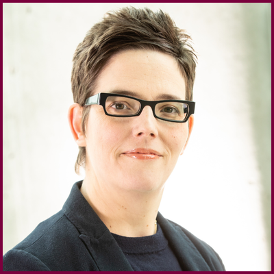 Headshot of Sara Bannerman, who has short-cropped dark hair, dark-framed glasses whose shirt and blazer are black.