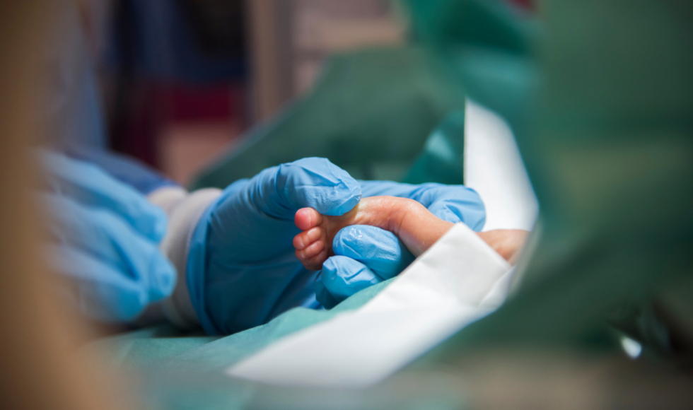 A gloved hand holds a baby's foot