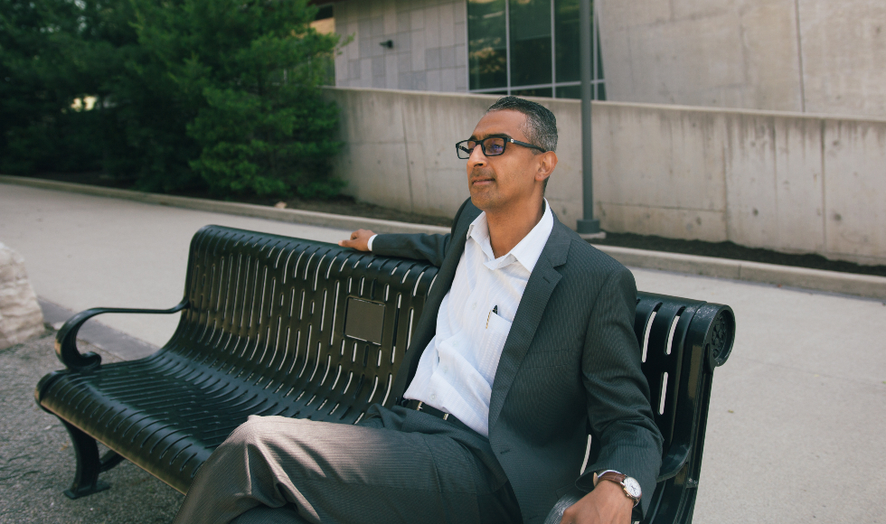 A man sits on a bench outside the W Booth School