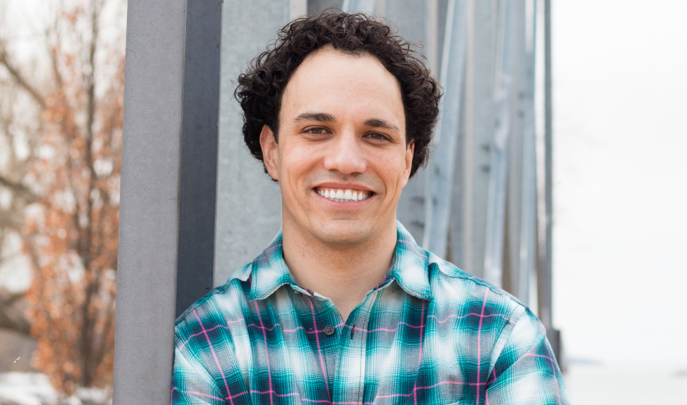 A smiling man stands in front of a metal monument