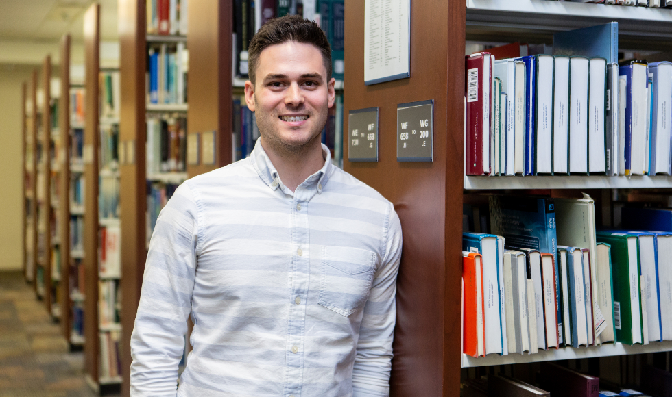 A man leans against a bookshelf in a library