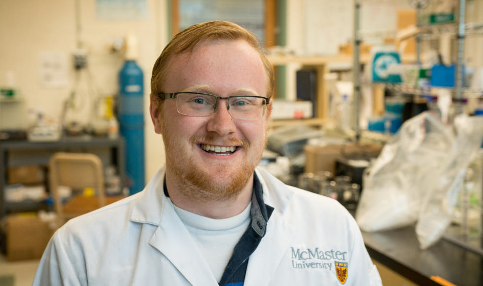 A man stands in a lab smiling and wearing a lab coat