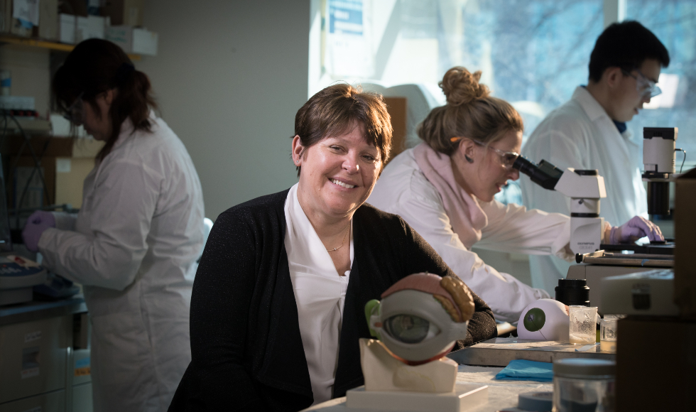 A smiling woman sits in fromt of a model of an eyeball