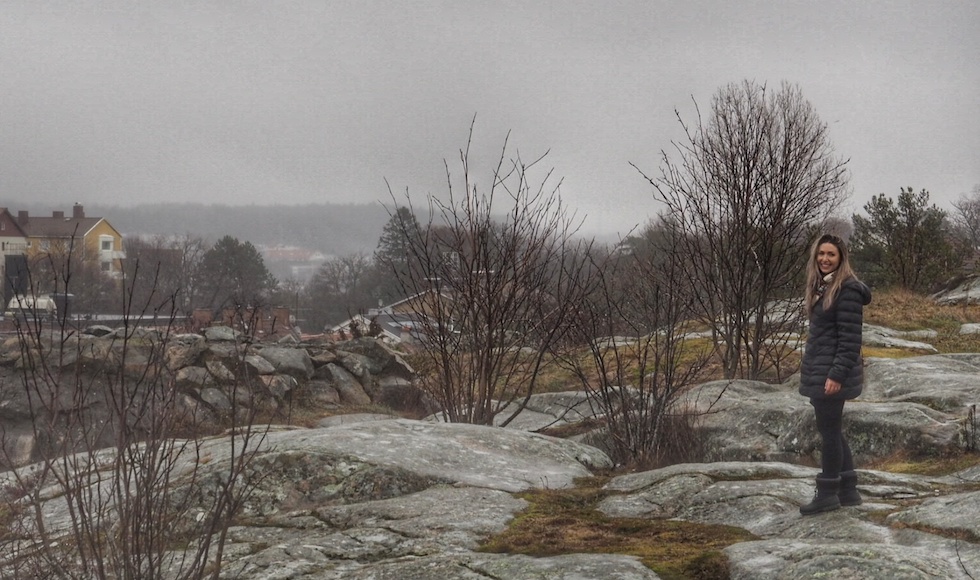 A woman stands on a rocky landscape with houses in the distance.