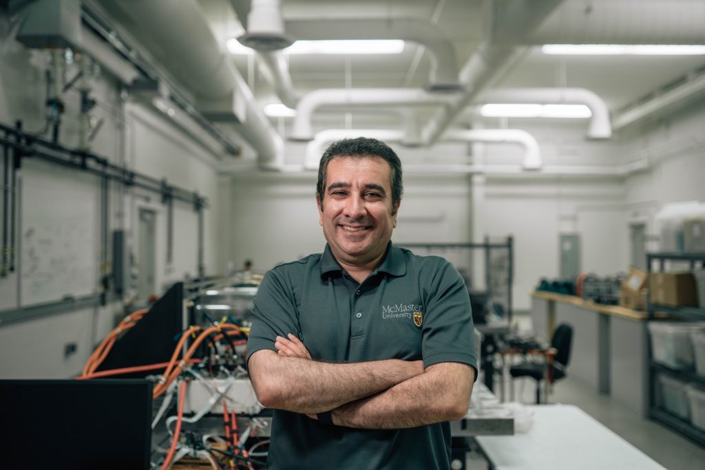 A man standing in a research lab with his arms crossed and smiling