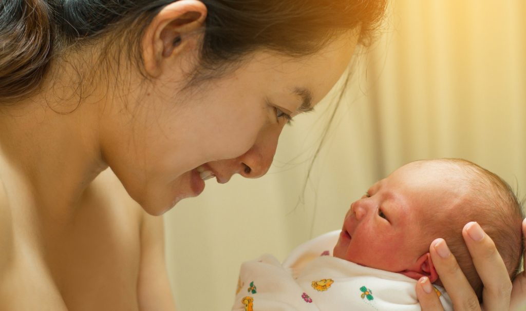 Woman smiling at a swaddled, alert newborn infant.