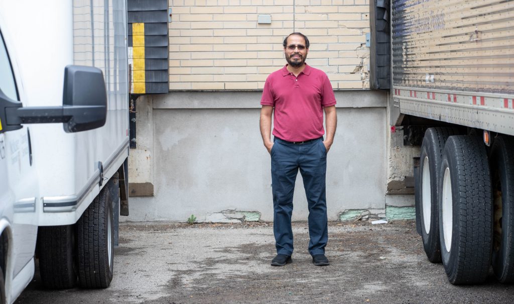 Elkafi Hassini standing in a loading area between two freight trucks.