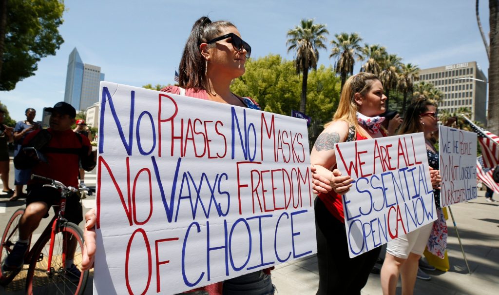 Protesters holding signs about vaccines and reopening at a protest in Sacramento.