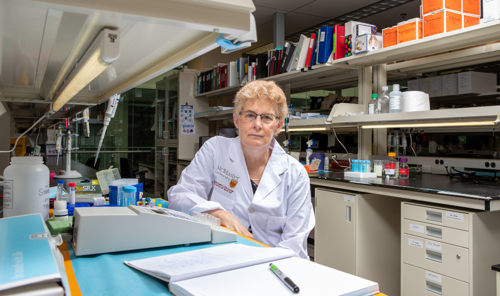 Photo of a woman in a lab coat, sitting at a lab table