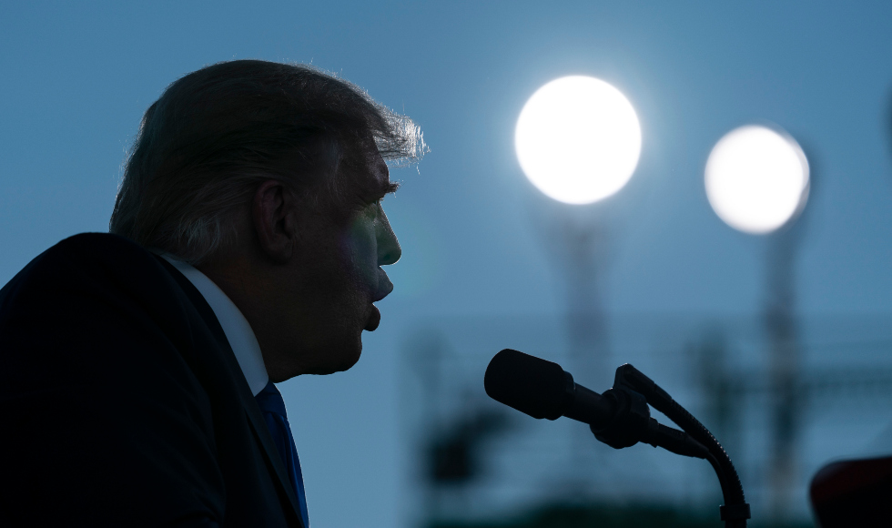 Donald Trump in close-up silhouette speaks into microphones