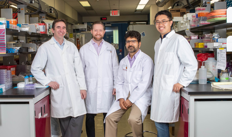 Four men in lab coats stand in a lab