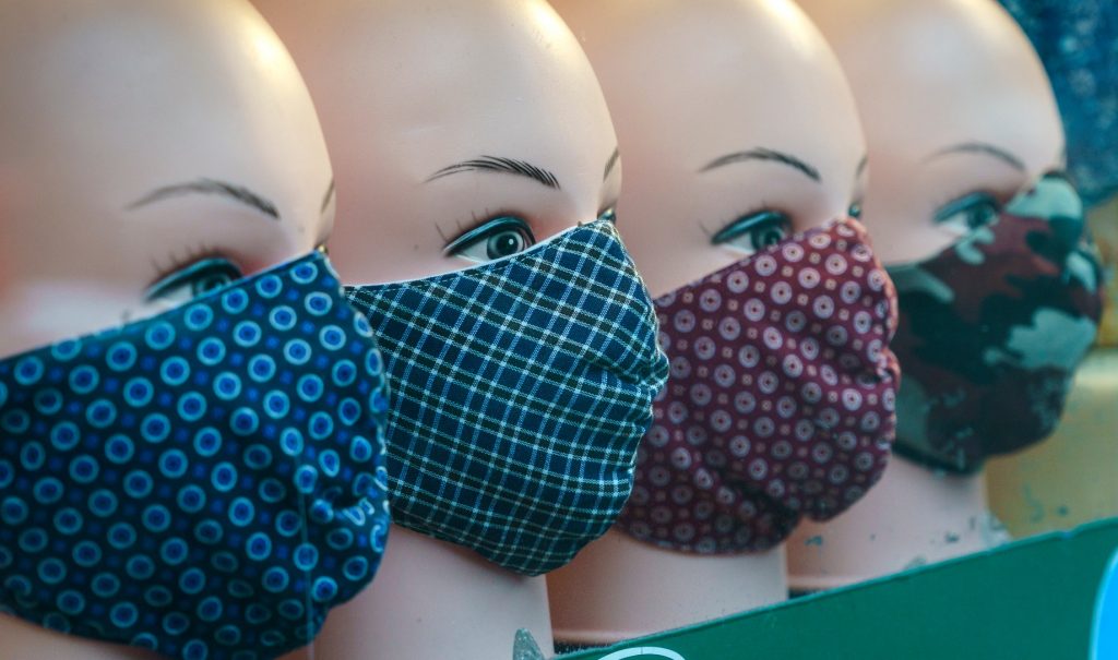 A closeup of a line of mannequin heads wearing patterned fabric masks.