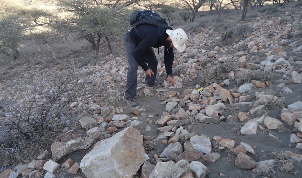 Julien Favreau is bending over to touch a rock. He's standing on a slope covered in rocks.