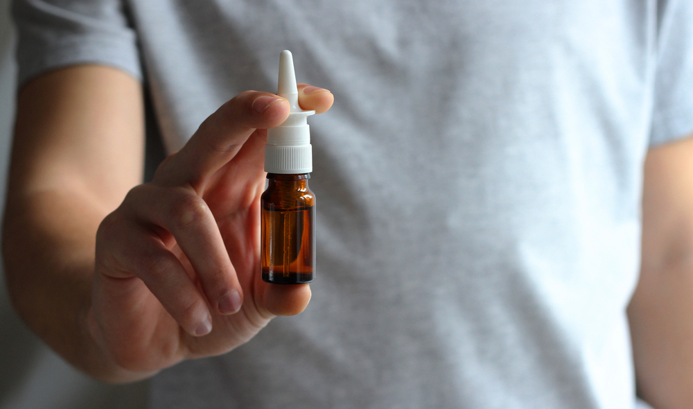 A man in a white t-shirt holds a bottle of nasal spray