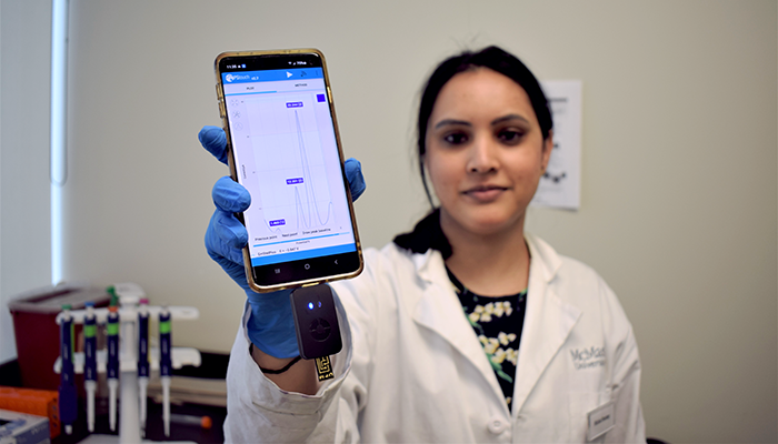 Richa Pandey in a lab coat, holding up a smartphone showing test results