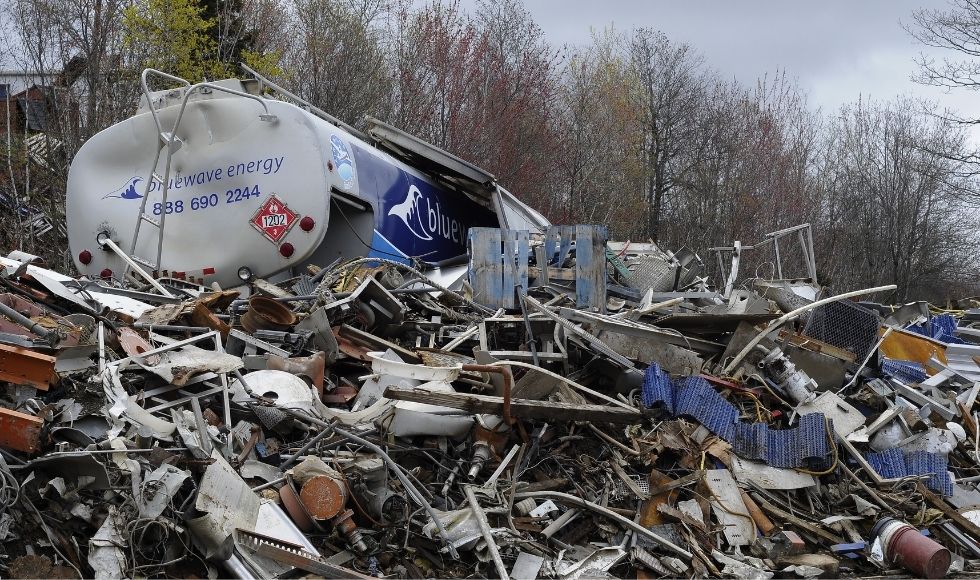 A tanker truck rest on a heap of other metal and wood waste in a dump.