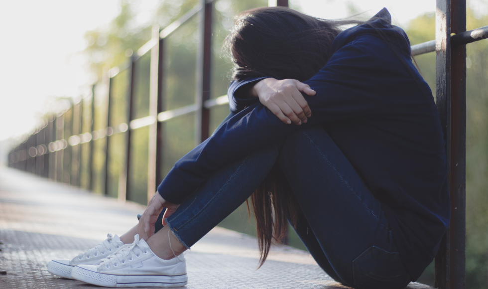 A photo of a woman sitting on the ground bent over with her head resting on her arms.