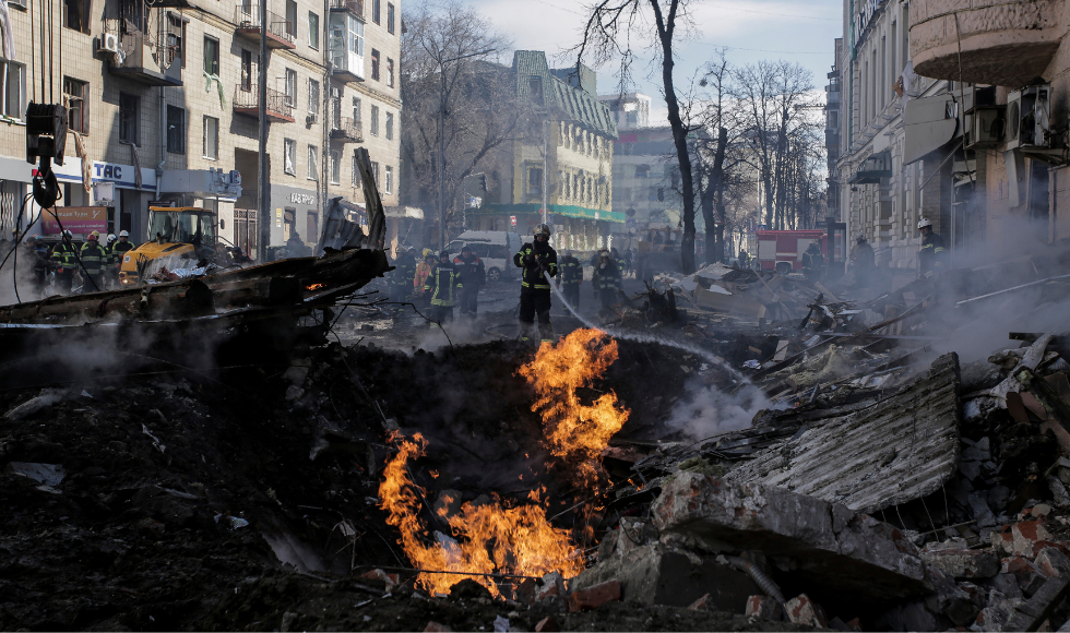 Firefighters point a hose at flames in the midst of the rubble of a destroyed building