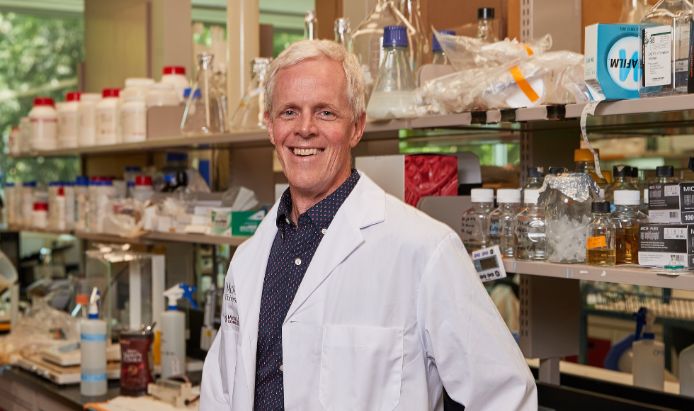 Eric Brown wearing a lab coat in a lab full of smiling