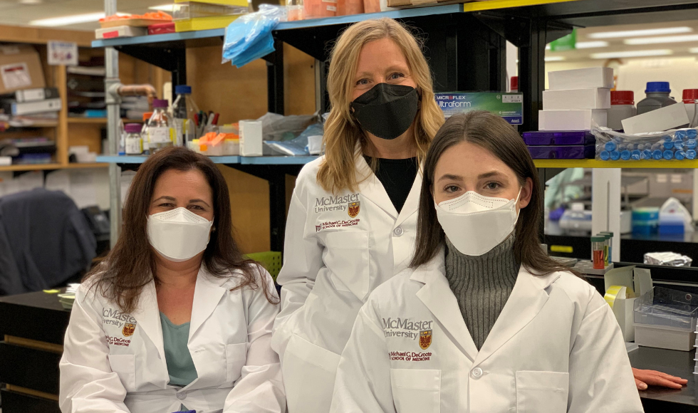 Three researchers in McMaster lab coats in a lab.