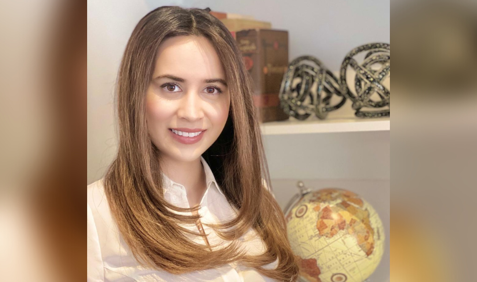 Marjan Walli-Attaei smiling at the camera. Behind her is a set of shelves with decorative items and a globe on them.