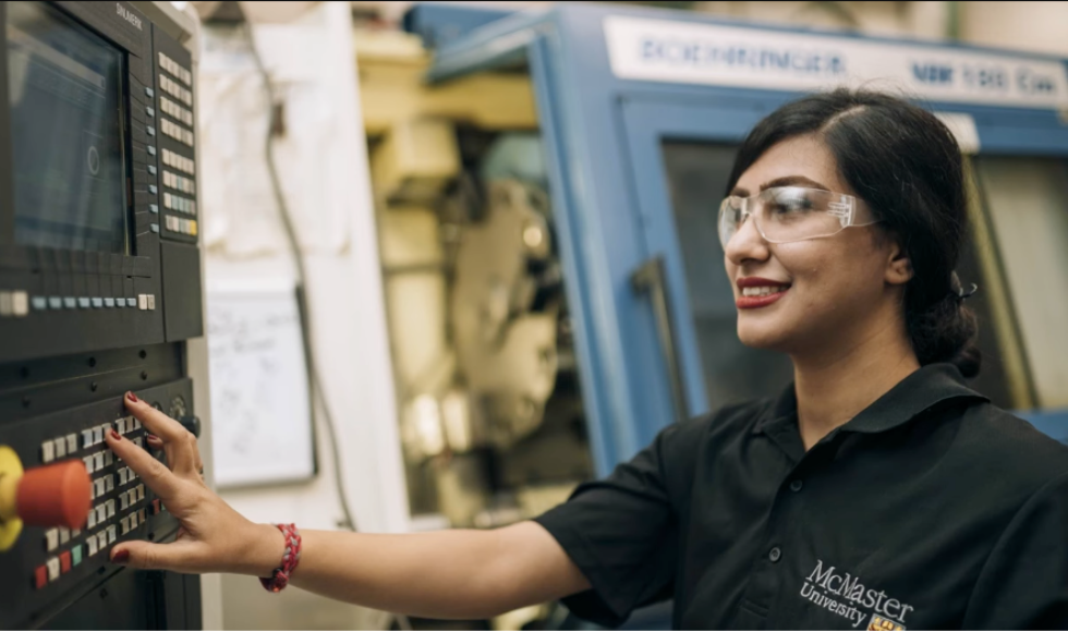 A student in safety goggles reaches out and touches an instrument panel.