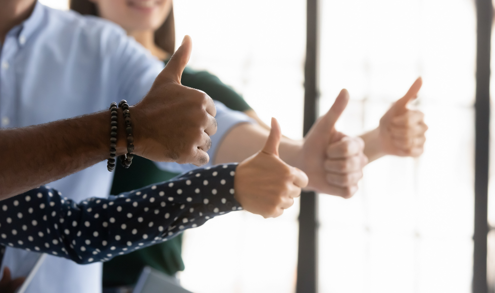 The arms of four people stretched out and with their hands in a 'thumbs up' position.