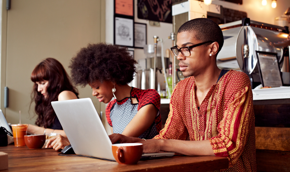 Three people sitting and working side by side at a table in a coffee shop.