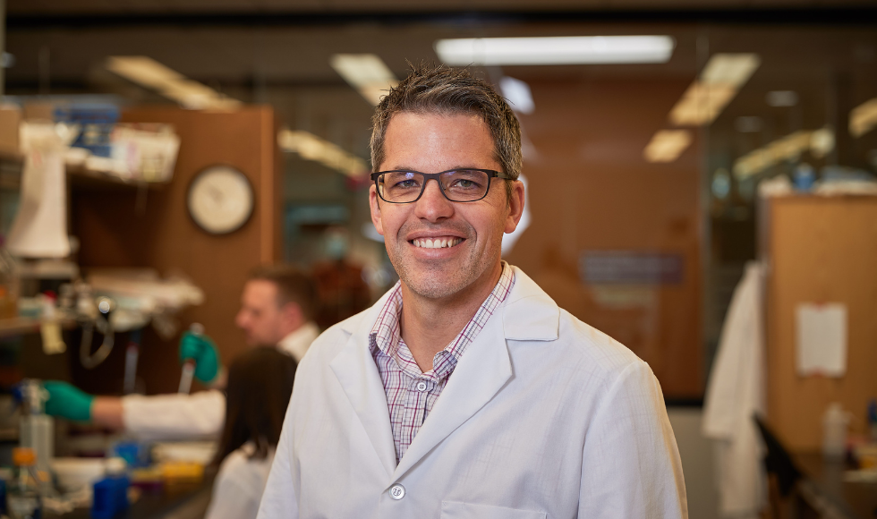 Brian Coombes wearing a white lab coat and smiling at the camera.