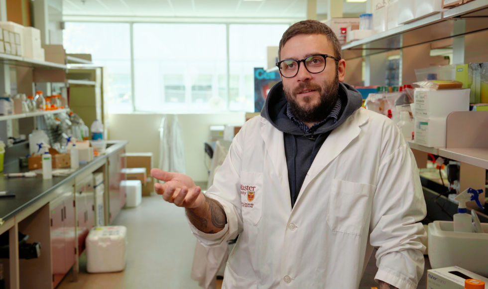 Jon Stokes wearing a white lab coat and standing in a laboratory setting