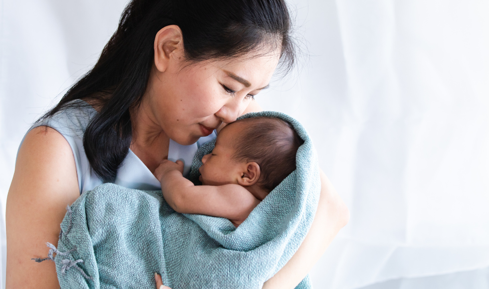 Woman snuggling new born in blanket