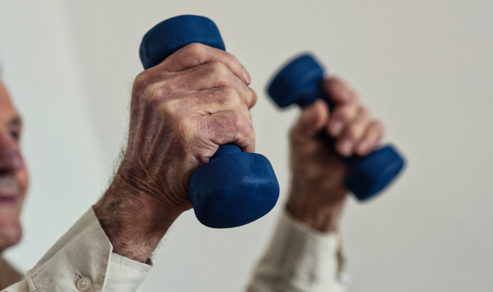 An elderly man holding up a pair of blue dumbbells