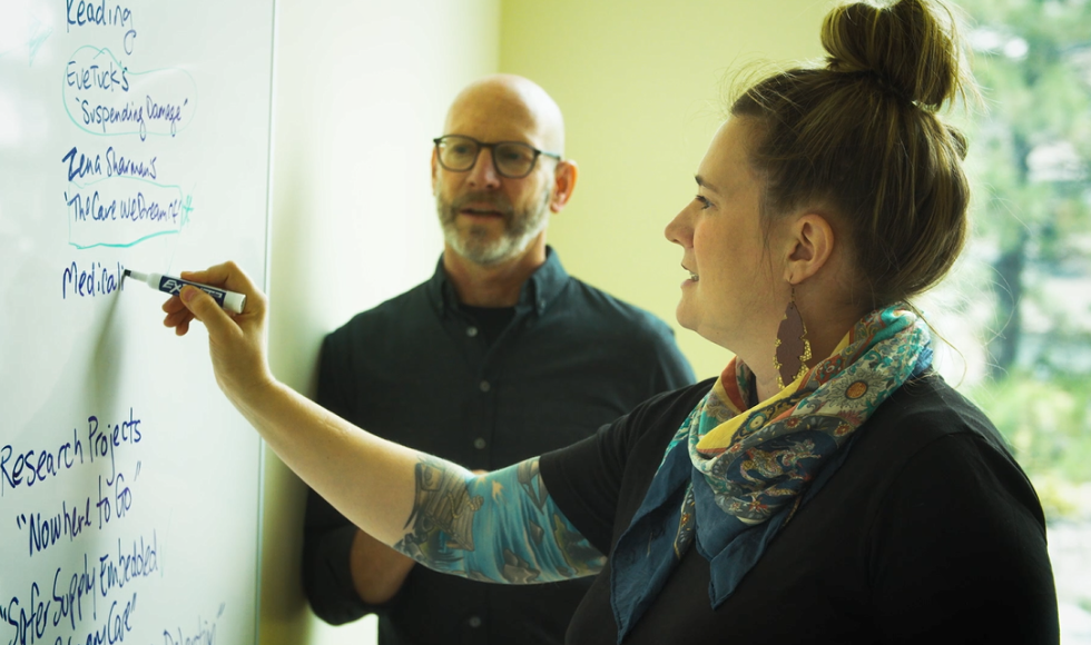 Claire Bodkin writes on a whiteboard while another person looks on