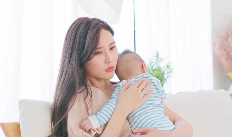 A glassy-eyed, sad-looking woman holding a baby.