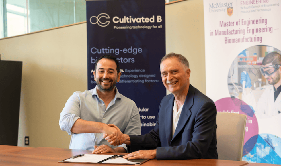 Two men seated at a desk smiling and shaking hands