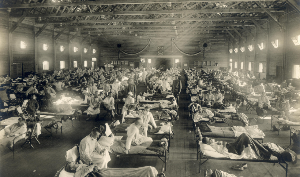 A black and white photo of an emergency hospital during the 1918 pandemic showing nurses taking care of sick patients.