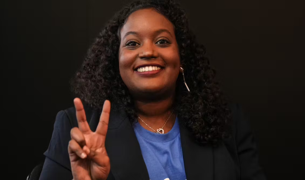 Sarah Jama smiling and making a V shape with her fingers against a dark background