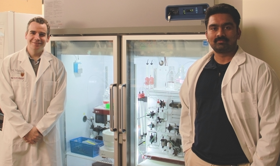 Two men in white lab coats standing on either side of laboratory equipment