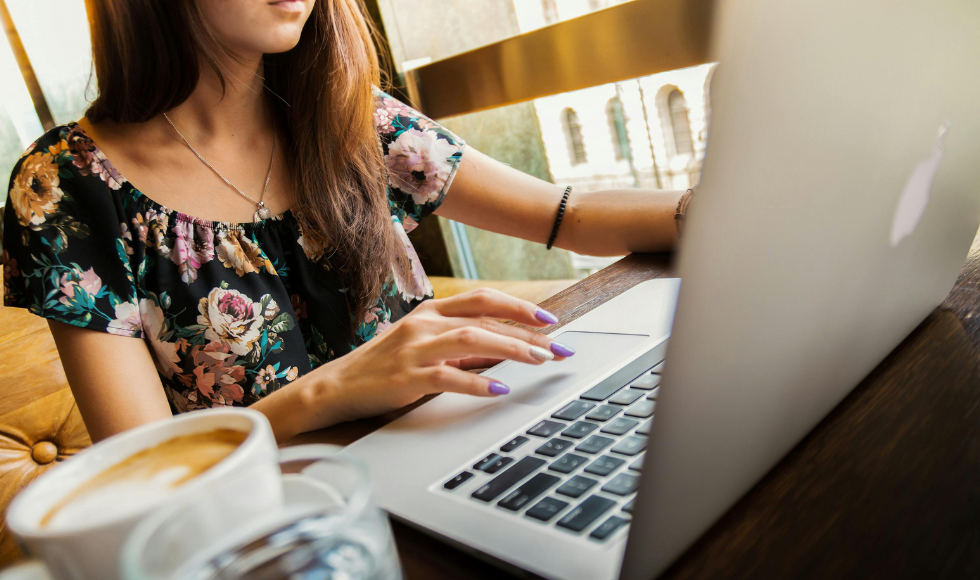 Image of someone sitting at a desk, with coffee by their side, and using their laptop