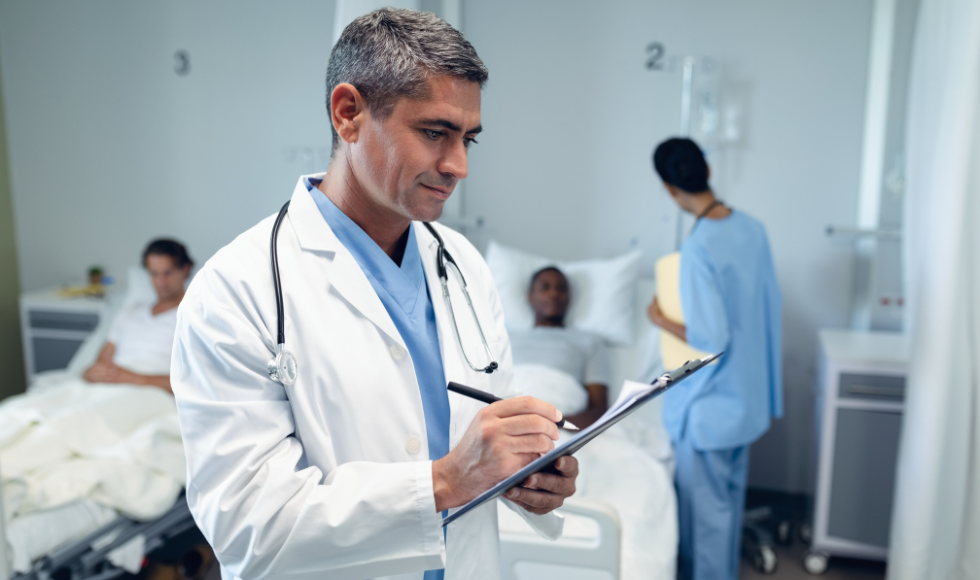 Image of a doctor writing on his chart in a hospital room