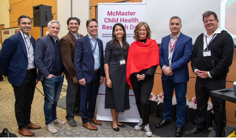 Eight McMaster researchers and other leaders standing in front of a sign for McMaster Child Health Research Day.