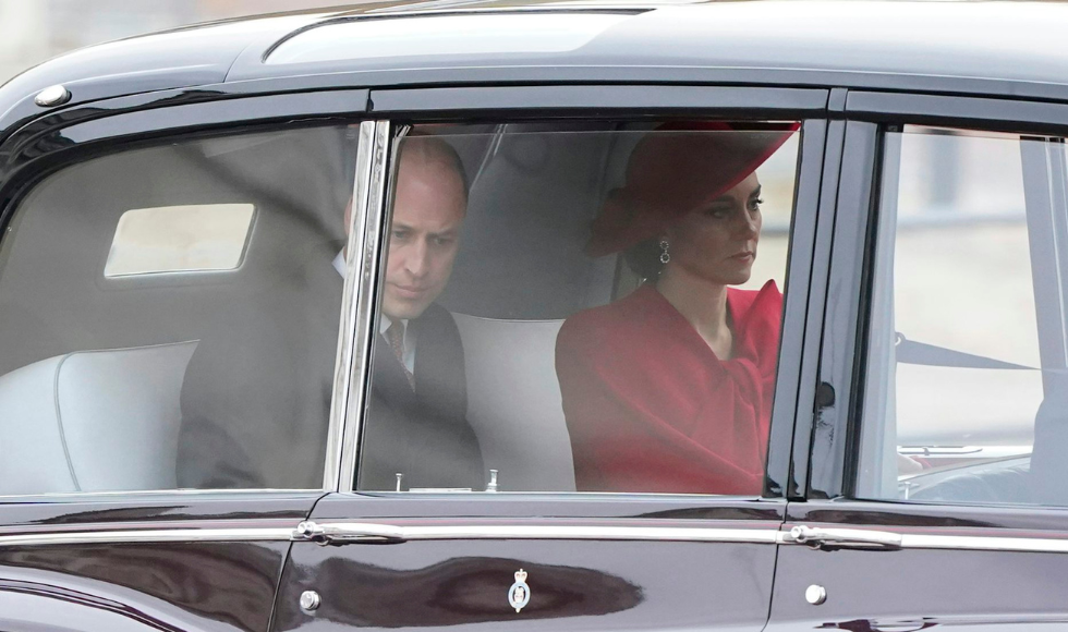 Prince and Princess of Wales sitting in the back seat of a car, seen through the window